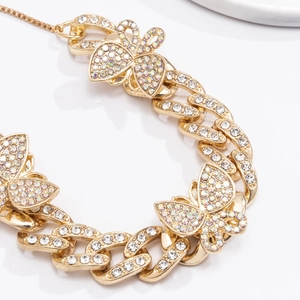 Macro detail of gold Cuban link anklet with diamond butterflies and iridescent rhinestones