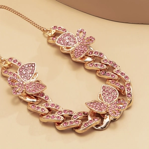 Detail of golden Cuban link anklet featuring pink rhinestone butterflies on a beige pedestal