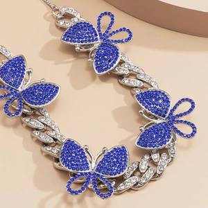 Macro detail of silver Cuban chain necklace featuring butterfly charms with blue rhinestones