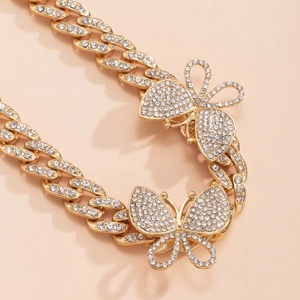 Close-up of hip hop gold Cuban link anklet with crystal butterfly pendants on peach background
