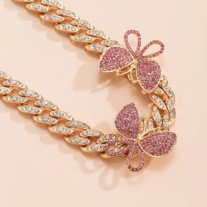 Macro detail of gold Cuban chain featuring pink rhinestone butterfly pendants