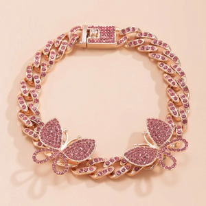 Macro detail of gold Cuban link butterfly anklet with pink rhinestones on pink background