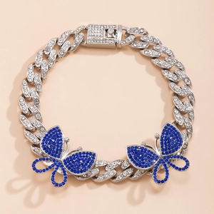 Close-up of iced out Cuban link anklet featuring two sparkling blue rhinestone butterflies