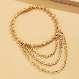 Macro detail of layered gold tassel anklet featuring sparkling rhinestone tennis chains