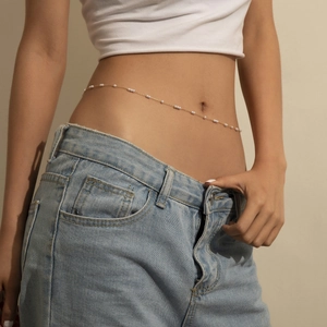 Dettaglio di una sottile catena dorata in vita con perle bianche su jeans denim