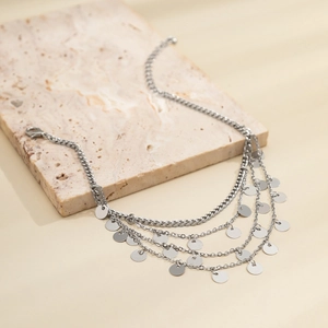 Close-up of multilayer silver tassel anklet with round metal charms on marble surface