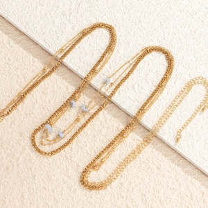 Detail of multilayer gold body chain featuring light blue stones and chunky Cuban links