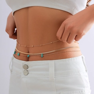 Detail of a layered gold waist chain featuring turquoise stones on a white outfit