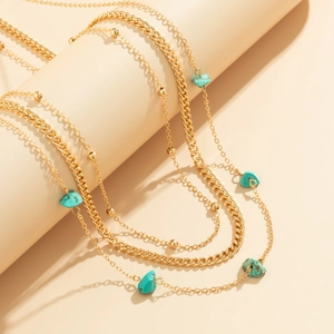 Close-up of layered gold alloy waist chains with turquoise stones on a beige pedestal