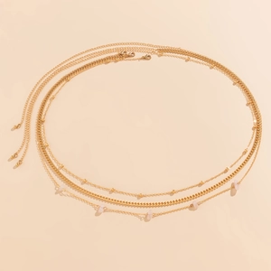 Close-up of multilayered gold body chain with pink stone accents on a peach background