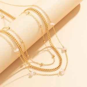 Detail of layered gold chains featuring pink natural stone chips and chunky cuban links