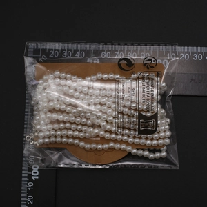 Vista de detalle de collar de perlas multicapa en cartón con regla de medición