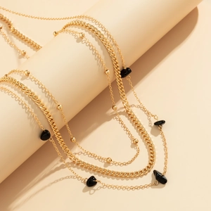 Close-up of layered gold chains with black stone accents on a minimalist display