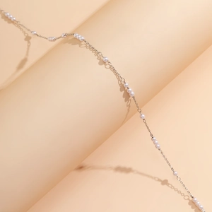 Dettaglio ravvicinato di una catena per il corpo in argento con delicate perle bianche