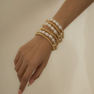 Detalle de un conjunto de pulseras multicapa de cuentas doradas y perlas blancas