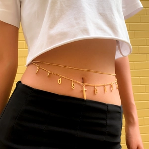Detail of layered gold waist chain with gothic letters and sword pendant on a model