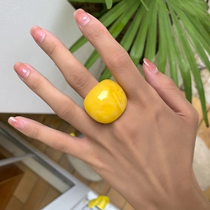 Nahaufnahme eines hellgelben Acrylrings mit Hochglanz-Finish an der Frauenhand