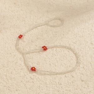 Detailed view of handmade beaded chain with red daisy flowers on stone surface