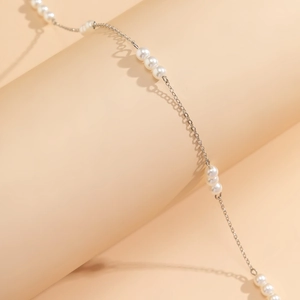 Dettaglio macro di catena corpo in perle argentate con maglie a cuore su fondo beige