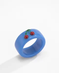 Detail eines blauen Harzrings mit zartem roten Kirschmotiv und grüner Blattverzierung
