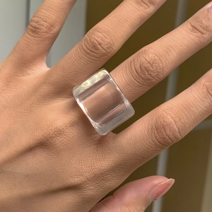 Détail macro d'une bague carrée en résine transparente portée montrant le style minimaliste