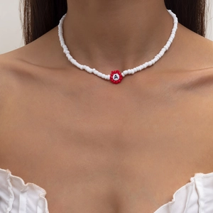 Primer plano de collar de cuentas blancas con colgante de flor roja y la letra A