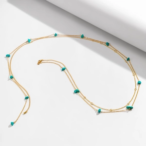 Detail of gold body chain with turquoise stones on white geometric props