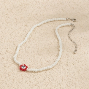 Detalle de collar de cuentas blancas con flor de perlas rojas y dije con la letra A