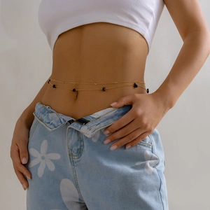 Detail of a double-layer gold waist chain with black stones worn on a model's waist