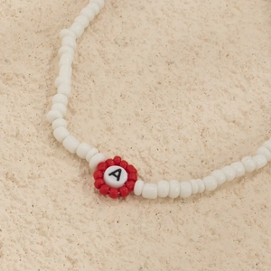Detalle de collar de cuentas hecho a mano con perlas blancas y flor roja con la letra A