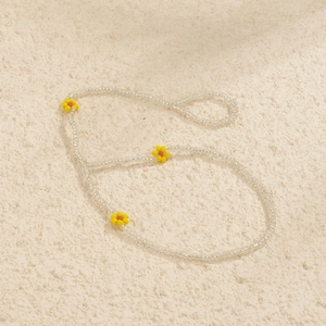 Detail of handmade beaded anklet with colorful daisy charms on textured stone
