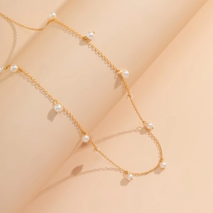 Dettaglio catena dorata per la vita con perle bianche su sfondo rosa minimalista curvo
