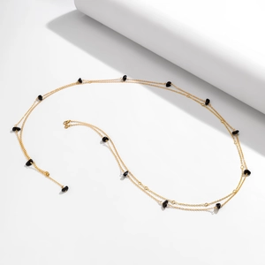 Detail view of a long gold body chain featuring black irregular stones for beach styling