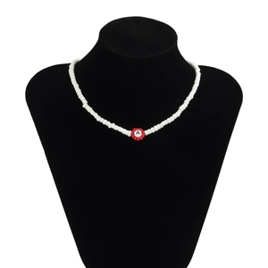 Detalle de collar de cuentas con flor roja y letra A sobre un busto negro