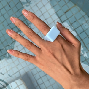 Gros plan d'une bague géométrique bleu clair en résine portée sur fond de piscine