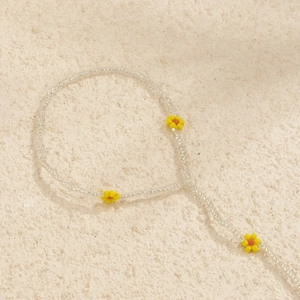 Close-up of handmade beaded daisy anklet with yellow flower accents on stone background