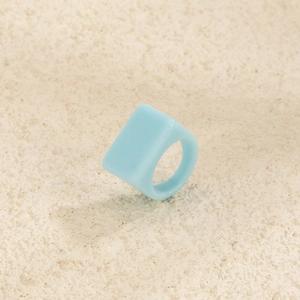 Détail d'une bague large en résine bleu clair avec dessus plat sur fond en pierre