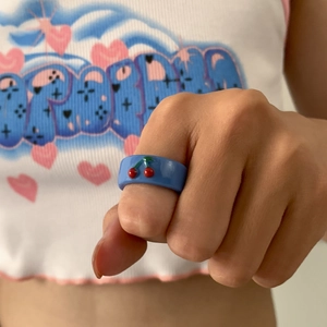 Nahaufnahme eines himmelblauen Harzrings mit roten Kirschen an der Hand eines Modells