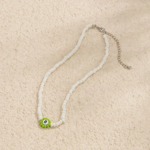 Detalle del collar de cuentas blancas con flor verde y colgante de letra B en negro
