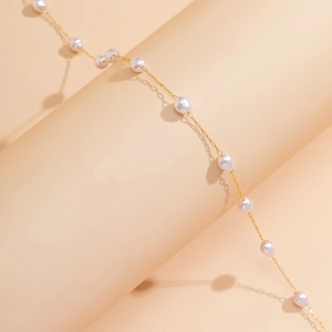 Dettaglio di un'elegante catena dorata con perle su un piedistallo beige sobrio