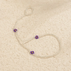 Close-up of bohemian beaded anklet featuring purple and yellow daisy flower charms