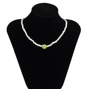 Detalle de collar de cuentas blancas con colgante de flor verde y letra B en un maniquí
