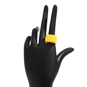 Détail d'une bague rectangulaire en résine jaune vif portée sur un présentoir de main