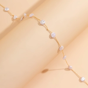 Dettaglio catena corpo dorata con eleganti perle barocche bianche su sfondo dai toni caldi