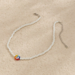 Detalle de collar de cuentas blancas con colgante de flor arcoíris y cuenta con letra C