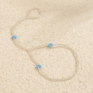 Detail of handmade beaded anklet with light blue and pink daisy charms on white sand