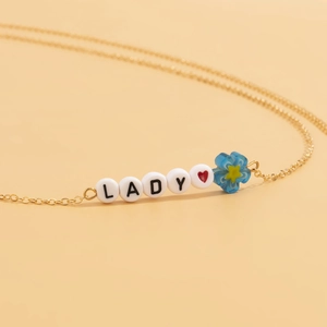 Λεπτομέρεια χρυσής αλυσίδας με χάντρες LADY και μπλε ακρυλικό λουλούδι