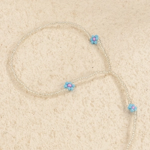 Detailed close-up of handmade bead anklet with blue daisy flowers on a textured background