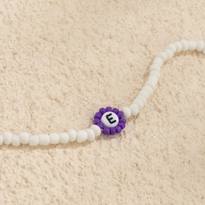 Detalle macro de joyería de cuentas blancas con flor púrpura y letra E en el centro
