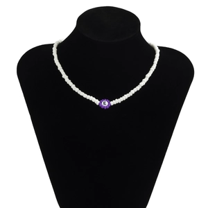 Detalle del collar de cuentas blancas de acrílico con un pétalo morado y la letra E central